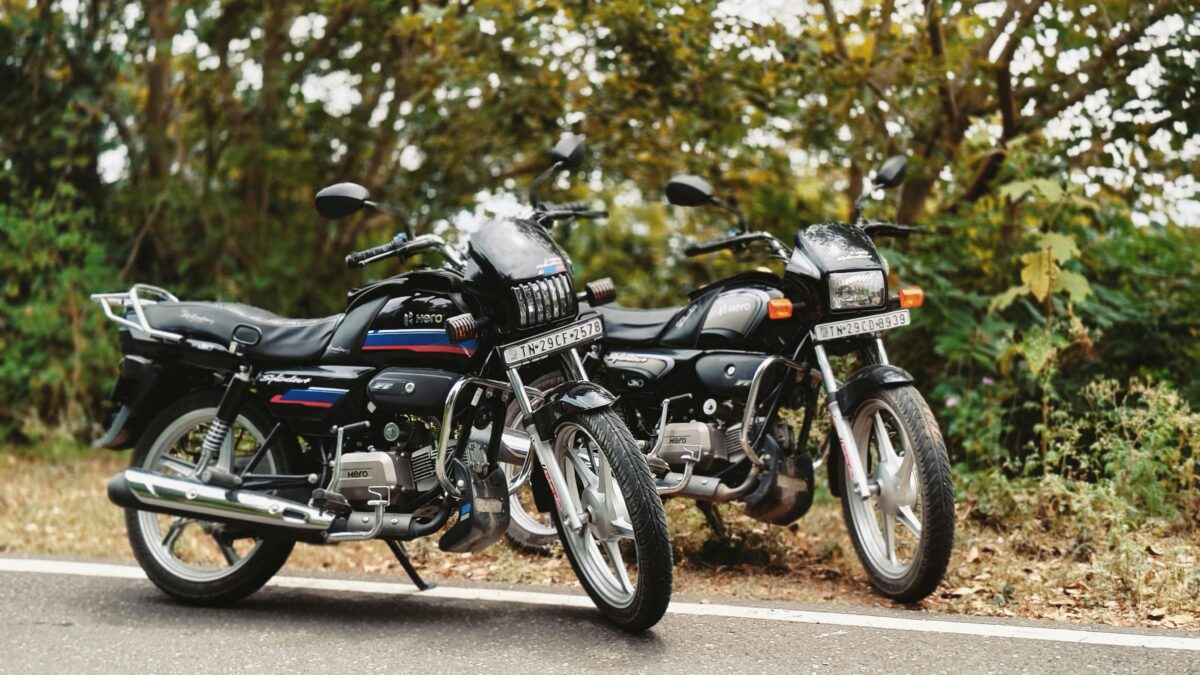 A promotional banner for "abtadka" featuring a lineup of four modern commuter motorcycles on a highway. The central text reads "BEST BIKES UNDER ₹1 LAKH IN INDIA 2026 | TOP PICKS, MILEAGE & PRICES." The image includes the abtadka logo, fuel pump icons, and rupee symbols, all set against a bright, scenic outdoor background.