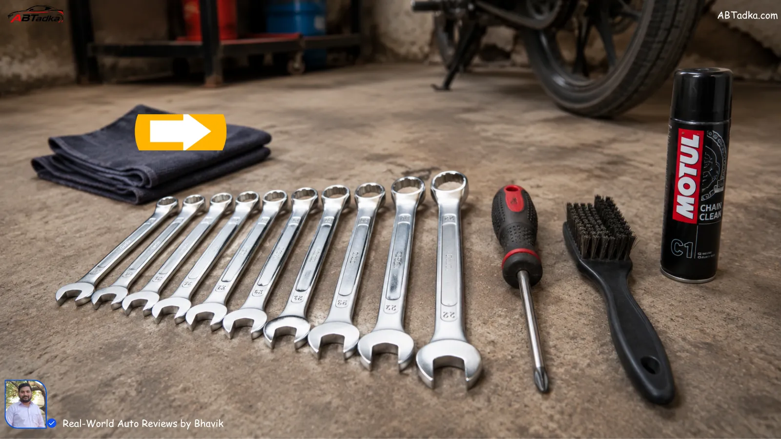 A basic tool kit including 10-12mm spanners, a screwdriver, and a cleaning brush on a garage floor.