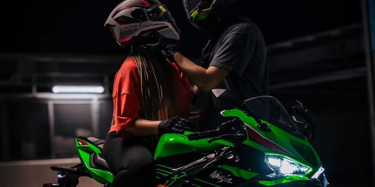 Two people on a green motorcycle preparing to ride at night.