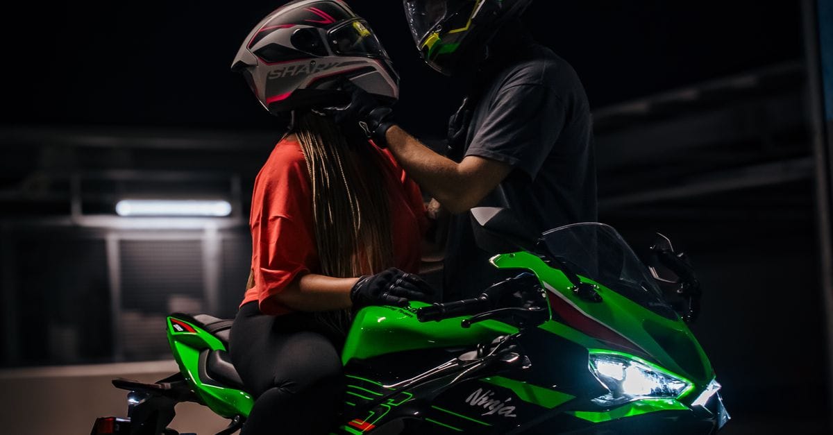 Two people on a green motorcycle preparing to ride at night.
