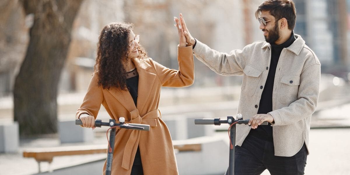 Happy couple sharing a high-five while enjoying a ride on electric scooters in an urban setting.
