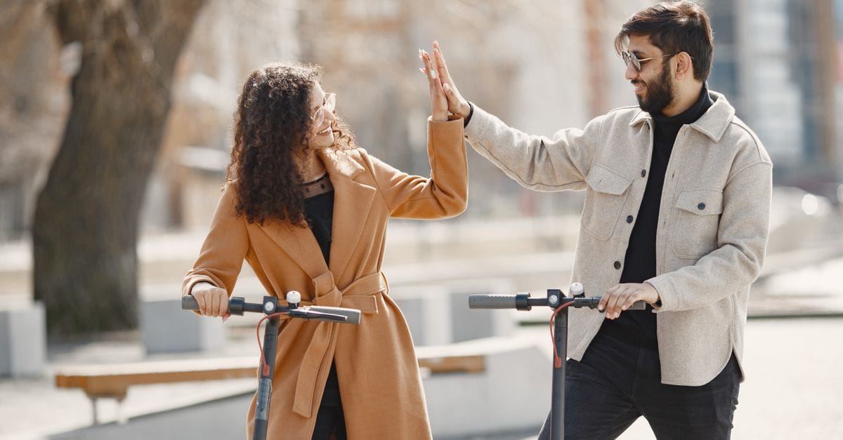 Happy couple sharing a high-five while enjoying a ride on electric scooters in an urban setting.